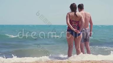 海滩夫妇从后面看海景。 一对夫妇站在白色的沙滩上度假，海浪飞溅